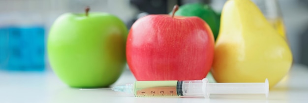 Apples and pear lying on table in laboratory near syringe with medicine closeup chemical