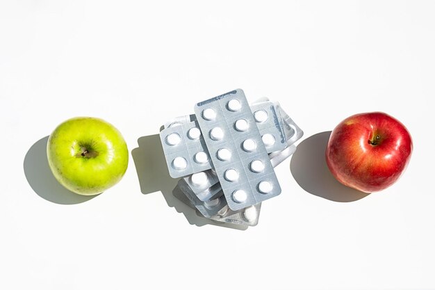 Apples and pills or vitamin capsules on white table copy space Wellness diet or supports for health concept