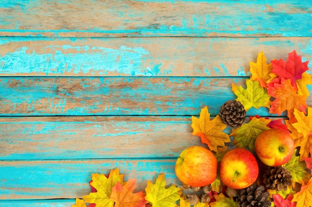 Photo apples and pine cones on wooden table over maple leaves.