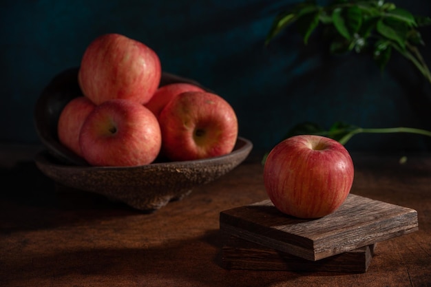 Яблоки на тарелке выглядят как картины маслом в тусклом свете на деревянном столе.
