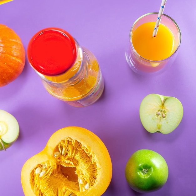 Apples, pumpkins, and juice on purple, top view