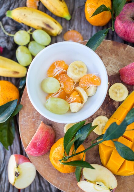 Apples tangerines bananas mangoes and grapes on a wooden board