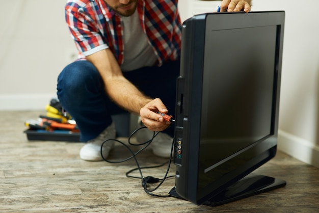 Photo appliance service cropped shot of repairman using a screwdriver while installing or fixing tv set