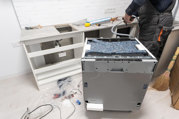 Appliance technician working under a kitchen sink installing a dishwasher.