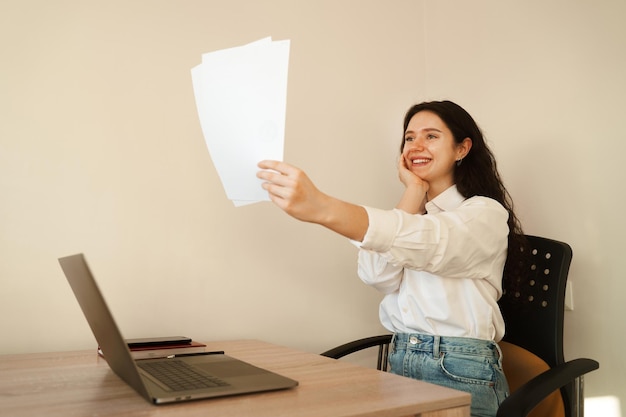 Applicant with laptop holds papers with exam results in his hands and rejoices Student girl passed exam and rejoices at high mark Online education and distance learning