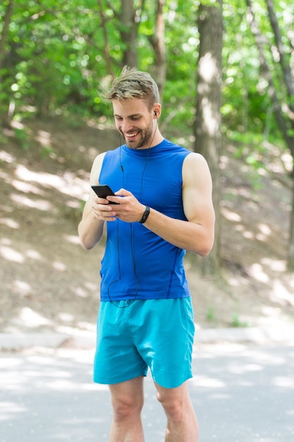 Applicatie instellen Sportman met smartphone en smartwatch voorbereiden op joggen Trainen met sportapplicatie is leuker Routeloop maken met applicatie Man smartphone klaar om te gaan joggen