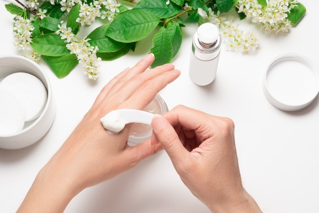 Apply hand cream with plastic spatula taking cream white table with bird cherry