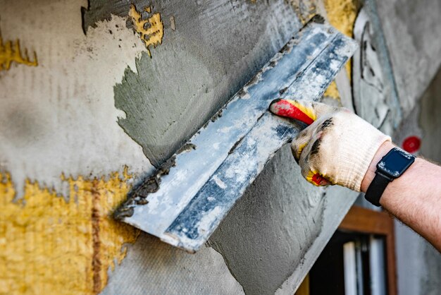 Нанесение слоя строительного клея на утепленную стену для укладки армирующей сетки из стекловолокна на минеральную вату.
