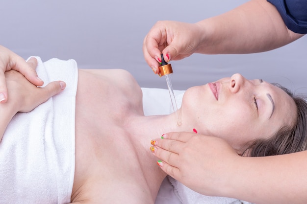 Applying essential oil with a pipette on the girl's neck to massage the face and neck. Anti-aging face and neck massage. Cosmetic care for face and neck skin