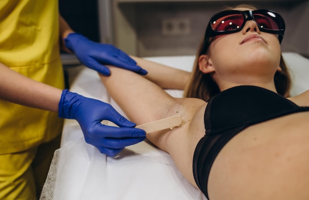 Applying hair removal gel under the arms Woman at a laser epilation session with a modern laser in a beauty studio