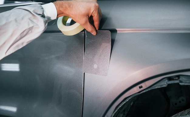 Applicazione di un nuovo colore il riparatore automobilistico caucasico in uniforme lavora in garage