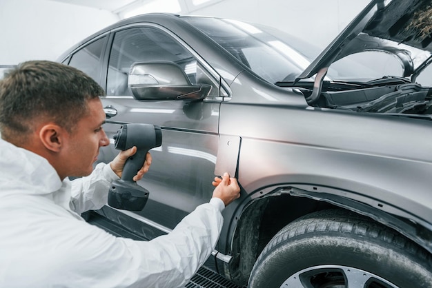 Applying new color Caucasian automobile repairman in uniform works in garage