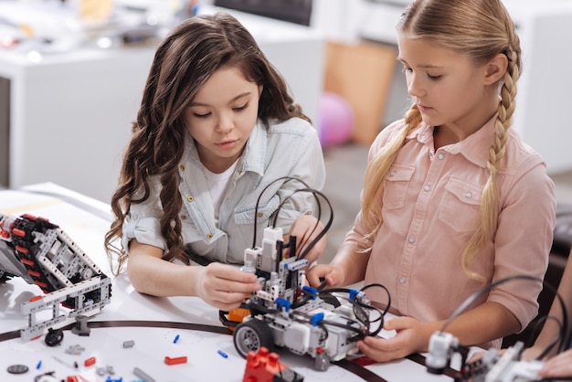 Applicazione di nuove informazioni. abili studentesse affascinanti intelligenti sedute a scuola e testando il cyber toy mentre hanno lezione di scienze