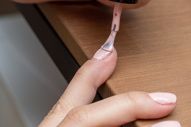 Applying pink nail polish gel, varnish with brush during manicure process