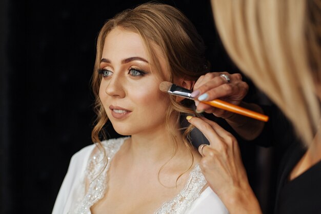 applying a with brush for applying blush. wedding makeup. Makeup artist paints lipstick girl. Make up artist  in process in.Beautiful woman face. with evening makeup. Hand of make-up master