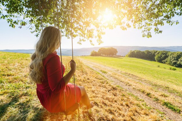 Foto appy giovane donna su un'altalena con vista sullo sfondo del tramonto e paesaggio