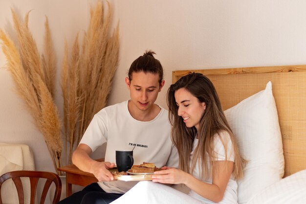 Apreciative young woman beacuse of her boyfriend surprised in bed happy couple having breakfast