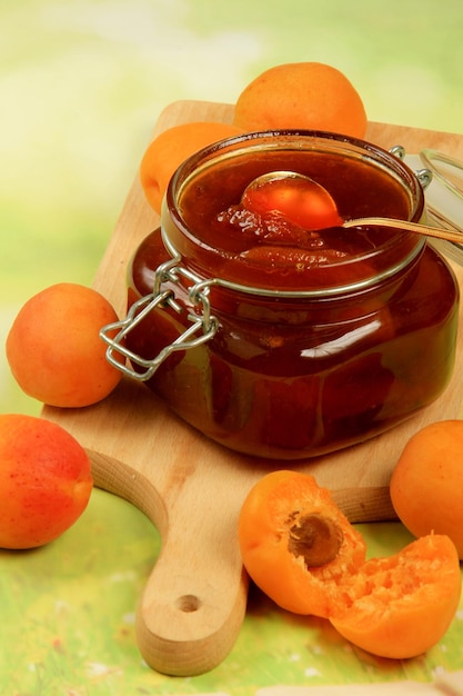 Apricot jam in a glass jar, fresh apricots on a light wooden background