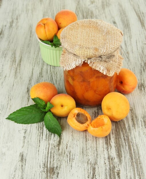 Apricot jam in glass jar and fresh apricots on wooden background