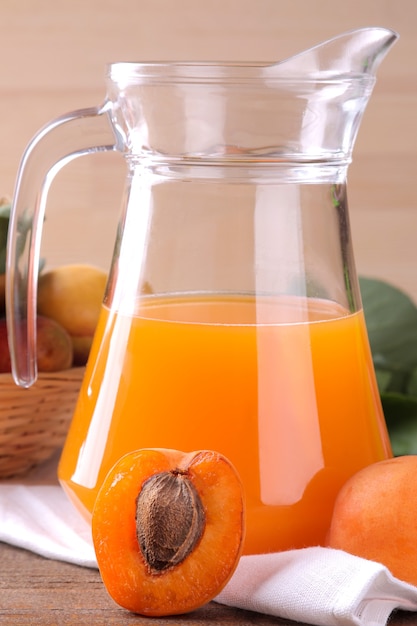 Photo apricot juice in a glass cup next to fresh apricots on a brown wooden table