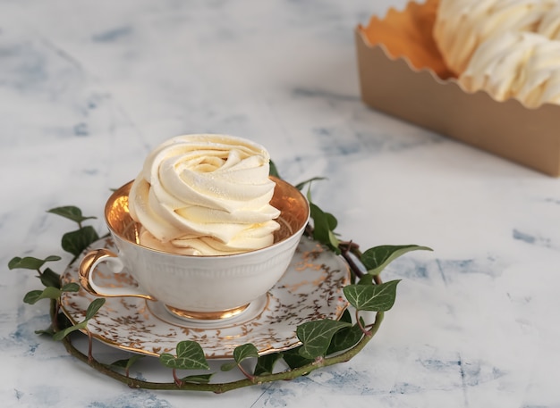 Photo apricot marshmallow in a cup surrounded by an ivy branch is located. homemade zephyr, close up.