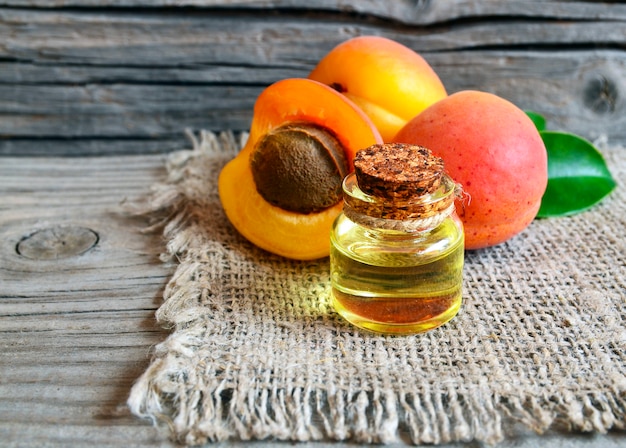 Apricot oil from apricot kernels in a glass jar and fresh ripe apricots on old wooden table.