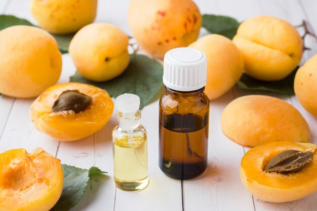 Apricot oil in a glass jar with fresh fruits close-up on the table.