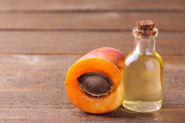 Apricot seed oil next to fresh apricots on a brown wooden table.