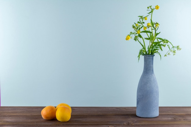 Apricots are on a wooden table. Vase with wildflowers on a blue background. Summer mood