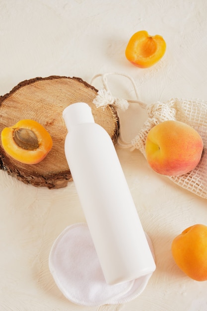 Apricots and a plastic white bottle mockup for cream or soap, a wooden podium from a saw cut made of wood on a light background top view