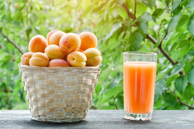 Apricots in a wicker basket and a glass of juice on a green background, sunlight