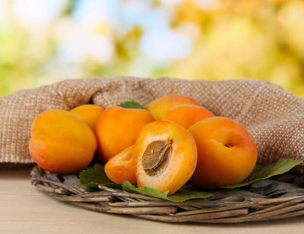 Apricots on wicker coasters on wooden table on nature background