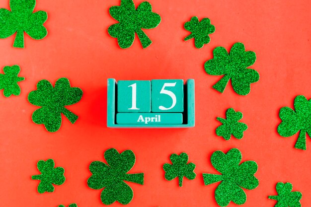 April 15 Blue cube calendar with month date and green clover leafs on bright orange background