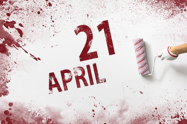 April 21st . Day 21 of month, Calendar date. The hand holds a roller with red paint and writes a calendar date on a white background. Spring month, day of the year concept.