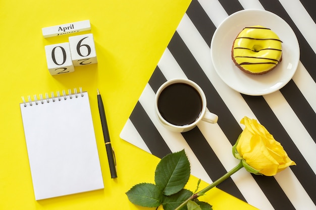 6 aprile. blocco note della rosa della ciambella della tazza di caffè su fondo giallo. luogo di lavoro elegante