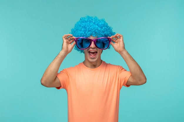 만우절 날 흥분한 남자 광대 핑크색 큰 선글라스 의상의 모서리를 잡고 재미있는 파란 머리