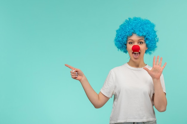 Фото Первоапрельский день девушка указывает на левый знак остановки с красным носом в костюме клоуна с синими волосами