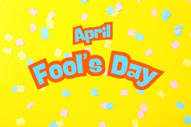 april fools day inscription and confetti on a yellow background top view
