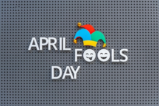 April Fools Day written on grey pegboard jester hat decorates the lettering on gray background