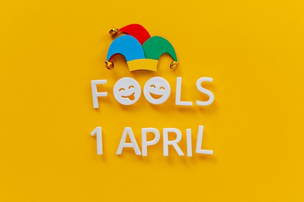 Photo april fools day over yellow background with jester hat first april card with laughing face