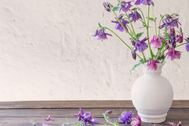 Aquilegia flowers in white vase on wooden table