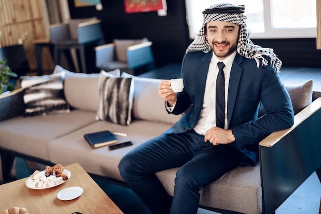 Arab businessman drinking coffee on couch at hotel room.