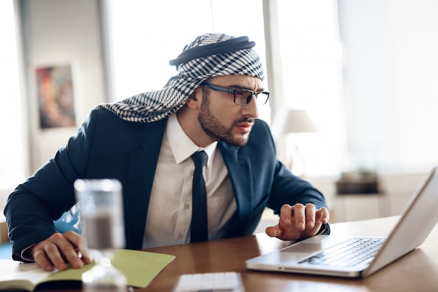 Arab businessman in suit taking notes at table at office.