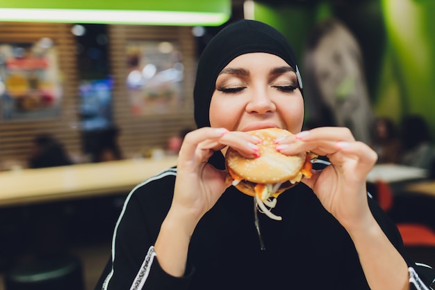 ハンバーガーを食べるファーストフードのレストランでアラブの女の子。