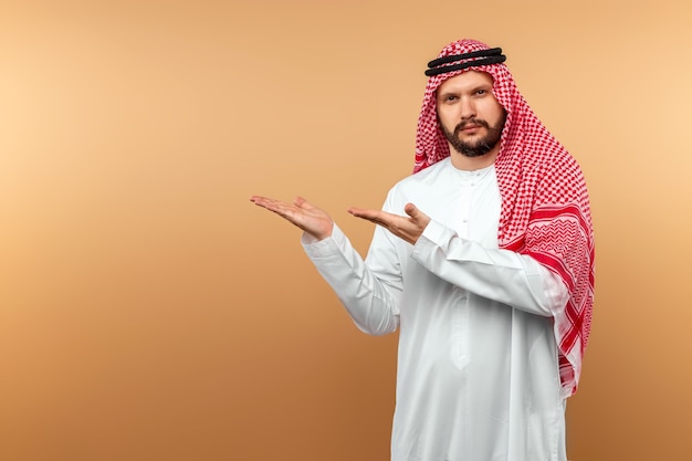 Arab male businessman in national clothes displays something, Beige wall.