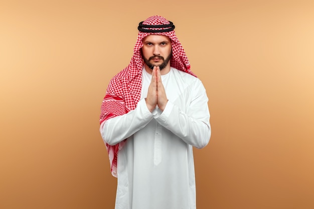 Arab man businessman in national clothes folded his hands in prayer, like, beige wall. 