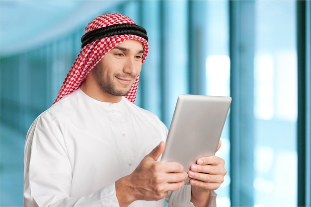 Arab man reading a tablet outdoor on a white wall