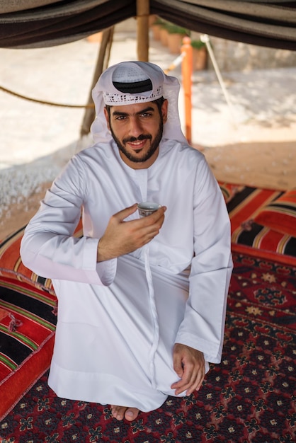 Arab man in traditional dress drinking arabic coffee in majilis