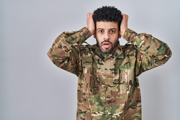 Arab man wearing camouflage army uniform crazy and scared with hands on head afraid and surprised of shock with open mouth