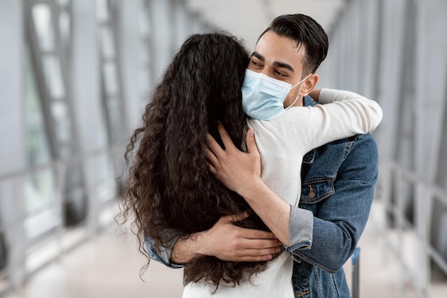 Arab man wearing medical mask embracing his girlfriend at airport after arrival